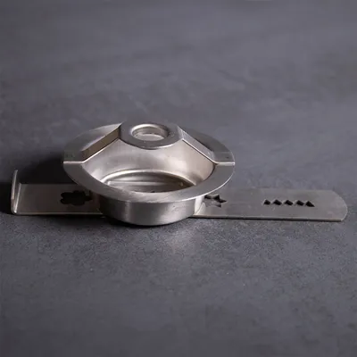 A silver metal cookie press attachment is shown on a dark gray surface.