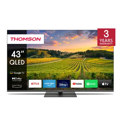 A Thomson 43" QLED TV is displayed on a stand, showcasing its screen which displays a vibrant landscape with vineyards and a sunset. The screen also shows app icons for Netflix, Prime Video, Disney+, YouTube, Spotify, and Apple TV.