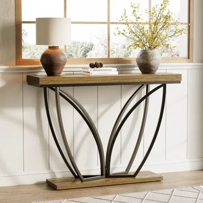 A console table with a lamp and vase of flowers on it, placed against a white paneled wall and a window.