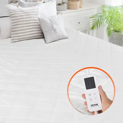 A person's hand is holding a white electric blanket controller on a white quilted mattress pad.