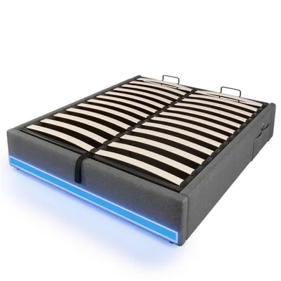 A grey upholstered bed frame with a slatted base, illuminated by blue LED lights around the bottom edge, shown from a diagonal angle against a white background.