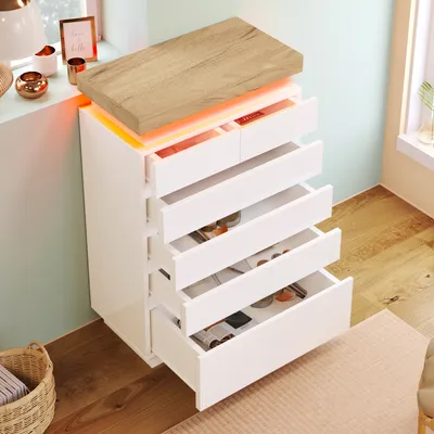 A white dresser with a wooden top and LED lighting, placed near a window with decorative items on the windowsill.