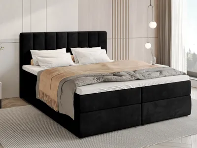 A black upholstered box spring bed with white bedding and a brown throw blanket is shown in a bedroom setting.