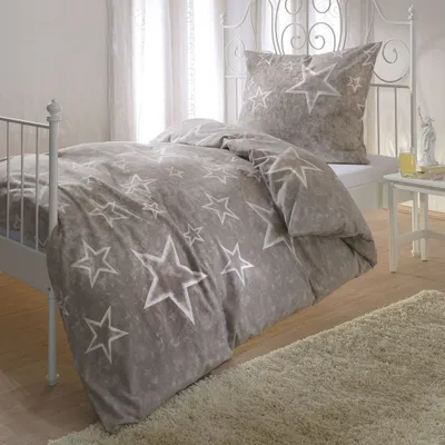 A bed with star-patterned bedding in a room with sheer curtains.