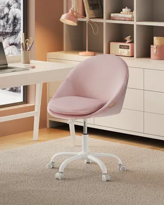 A pink velvet office chair sits on a rug in front of a desk and a bookshelf.