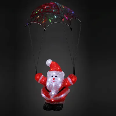 A lit-up acrylic Santa Claus figure with a parachute, against a dark background.
