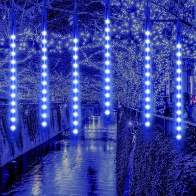 Blue LED meteor shower lights hanging over a canal at night, with trees and buildings in the background.