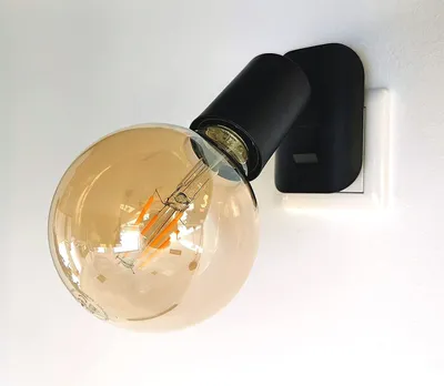A close-up shot of a black wall-mounted light fixture with a large, amber-colored Edison-style LED bulb.