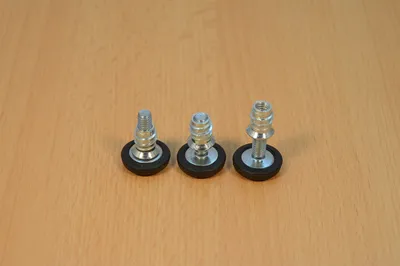 Three adjustable furniture feet with threaded bolts and rubber bases are arranged in a row on a wooden surface.