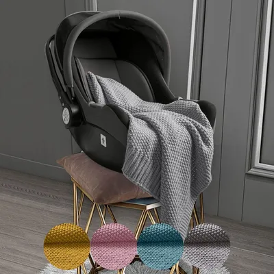 A baby car seat with a gray knitted blanket draped over it, placed on a stool. Four circular swatches of different colored blankets are shown at the bottom.
