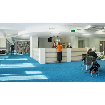 People in a library or community center setting, with bookshelves and a reception desk.