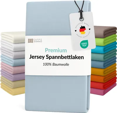 A stack of folded bed sheets in various colors, with a light blue sheet prominently displayed in the foreground with a product tag attached.