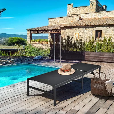 A sun lounger with a hat and a basket on a wooden deck next to a swimming pool, with a stone house in the background.