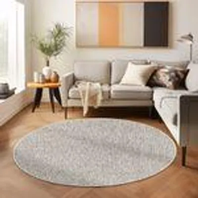 A round, beige rug in a modern living room setting with a sofa and side table.