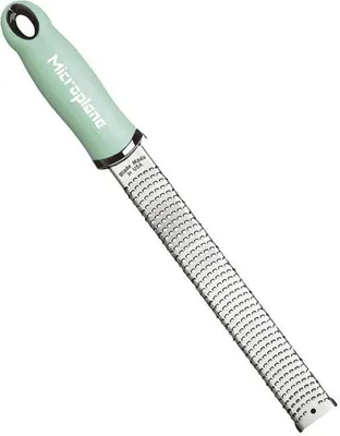 A close-up studio shot of a green and silver Microplane grater against a white background.