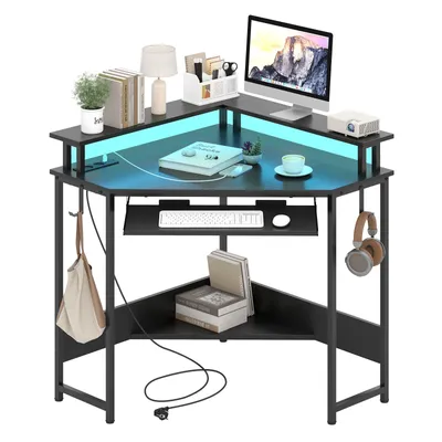 A black corner desk with a computer, keyboard, books, and decorative items, illuminated by blue LED lights.