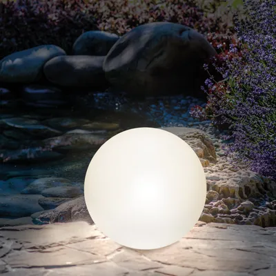 A glowing white sphere sits on a stone patio in a garden setting with rocks and lavender.