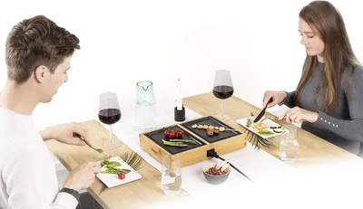 A couple is having dinner at a table, using a tabletop grill.