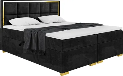 A black upholstered boxspring bed with a gold frame and headboard, shown with white pillows and a grey throw blanket.
