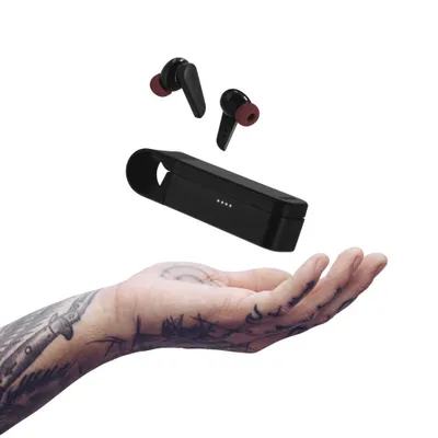 A hand with tattoos is holding a charging case and earbuds.