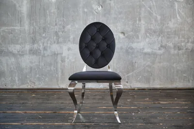 A black velvet chair with silver legs stands against a textured gray wall and dark wooden floor.