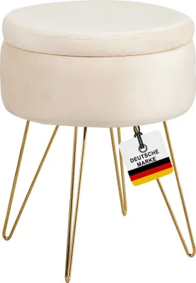 A beige upholstered stool with gold hairpin legs, featuring a tag with the German flag and text.