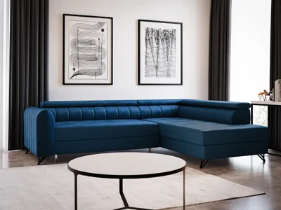 A blue sectional sofa is shown in a well-lit living room with two framed abstract art pieces on the wall and dark curtains.