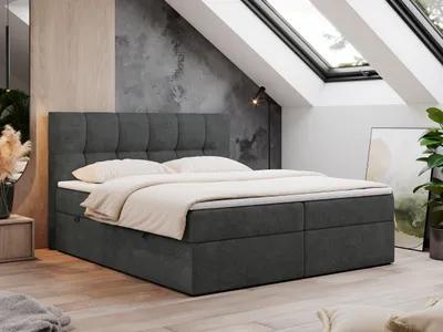 A dark gray boxspring bed with a tufted headboard is set up in a room with a sloped ceiling and skylights.