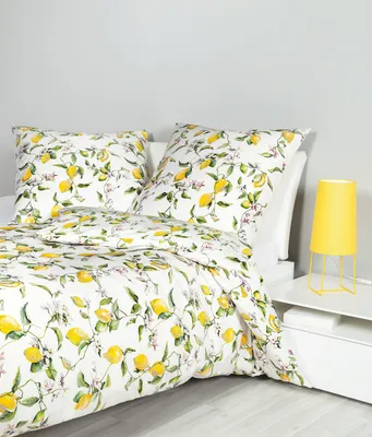 A bed with a lemon-patterned duvet and pillows, next to a bedside table with a yellow lamp.