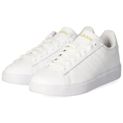A pair of white Adidas sneakers with gold accents.