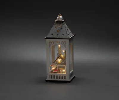 A decorative Christmas lantern with a miniature scene inside, set against a dark gray background.