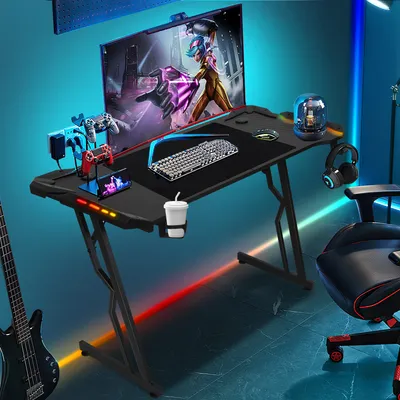 A gaming desk setup with a computer, keyboard, mousepad, headphones, and gaming controllers, illuminated by colorful LED lights.