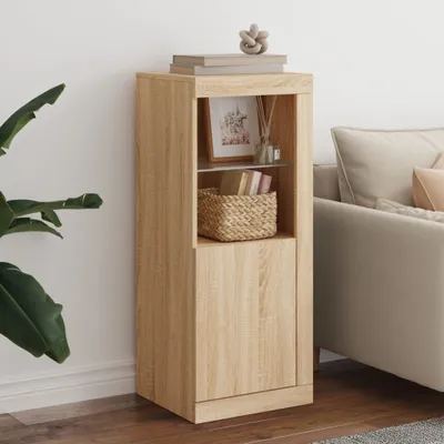 A wooden sideboard with a glass shelf and a cabinet door, decorated with books, a framed picture, and a basket, placed next to a sofa and a large plant.