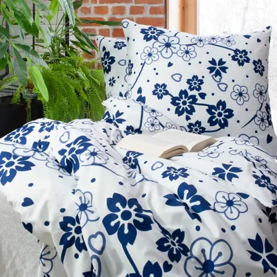 A bed with blue and white floral patterned bedding, pillows, and an open book.
