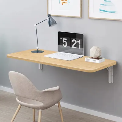 A wall-mounted folding desk with a laptop, lamp, and chair.