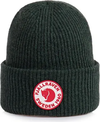 A close-up studio shot of a dark green knitted beanie with a circular red and white logo patch on the front.