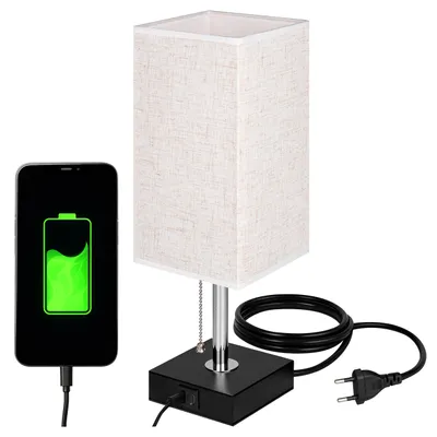 A bedside lamp with a smartphone charging next to it.