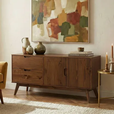 A wooden sideboard with two doors and two drawers, decorated with vases and books, in a room with a painting on the wall.