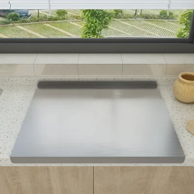 A stainless steel cutting board is placed on a kitchen countertop, with a window view of a garden in the background.