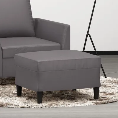 A gray ottoman is placed on a fluffy rug in front of a gray sofa. A floor lamp is visible in the background.
