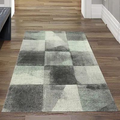 A rug with an abstract checkered pattern is placed on a wooden floor in a hallway.