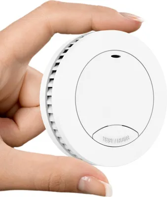 A hand holding a small, white smoke detector.