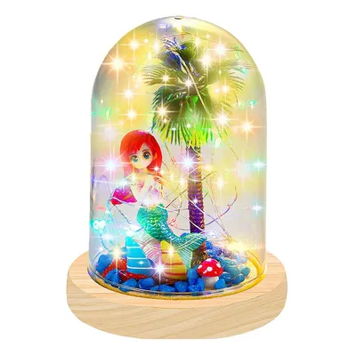 A decorative glass dome with a mermaid figurine, a palm tree, and fairy lights inside, resting on a wooden base.