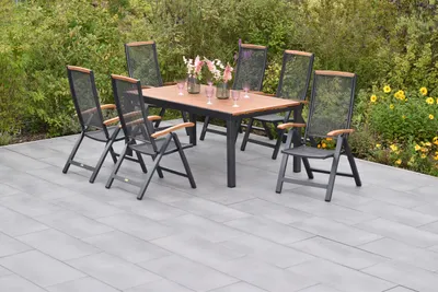 An outdoor dining set with a table and chairs on a patio, surrounded by greenery and flowers.