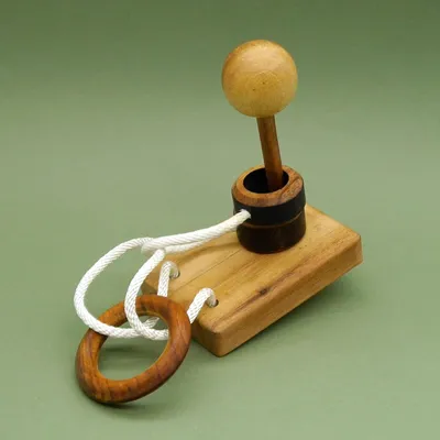 Laterne Seilpuzzle: Holzkugel auf Stab über dunklem Ring, weißes Seil verbindet Sockel mit hölzernem Ring.