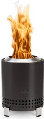 A dark gray Solo Stove Mesa with a silver rim and legs, with a bright orange flame burning inside.