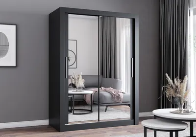 A modern bedroom with a large black wardrobe with mirrored doors, reflecting a living room area with a sofa and coffee table.
