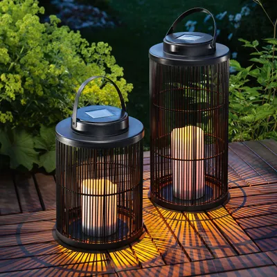 Two solar-powered lanterns with LED candles are placed on a wooden deck at dusk, casting patterned shadows.