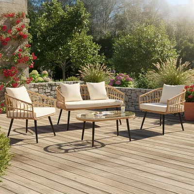 A rattan garden lounge set with a coffee table on a wooden deck, surrounded by plants and a stone wall.