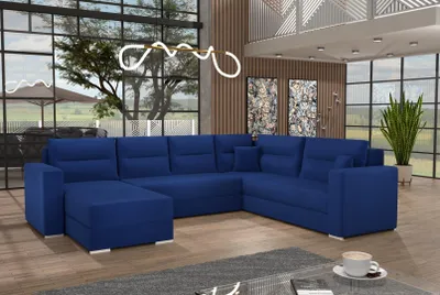 A large, deep blue sectional sofa is arranged in a modern living room with large windows, abstract art on the wall, and a tall potted plant.